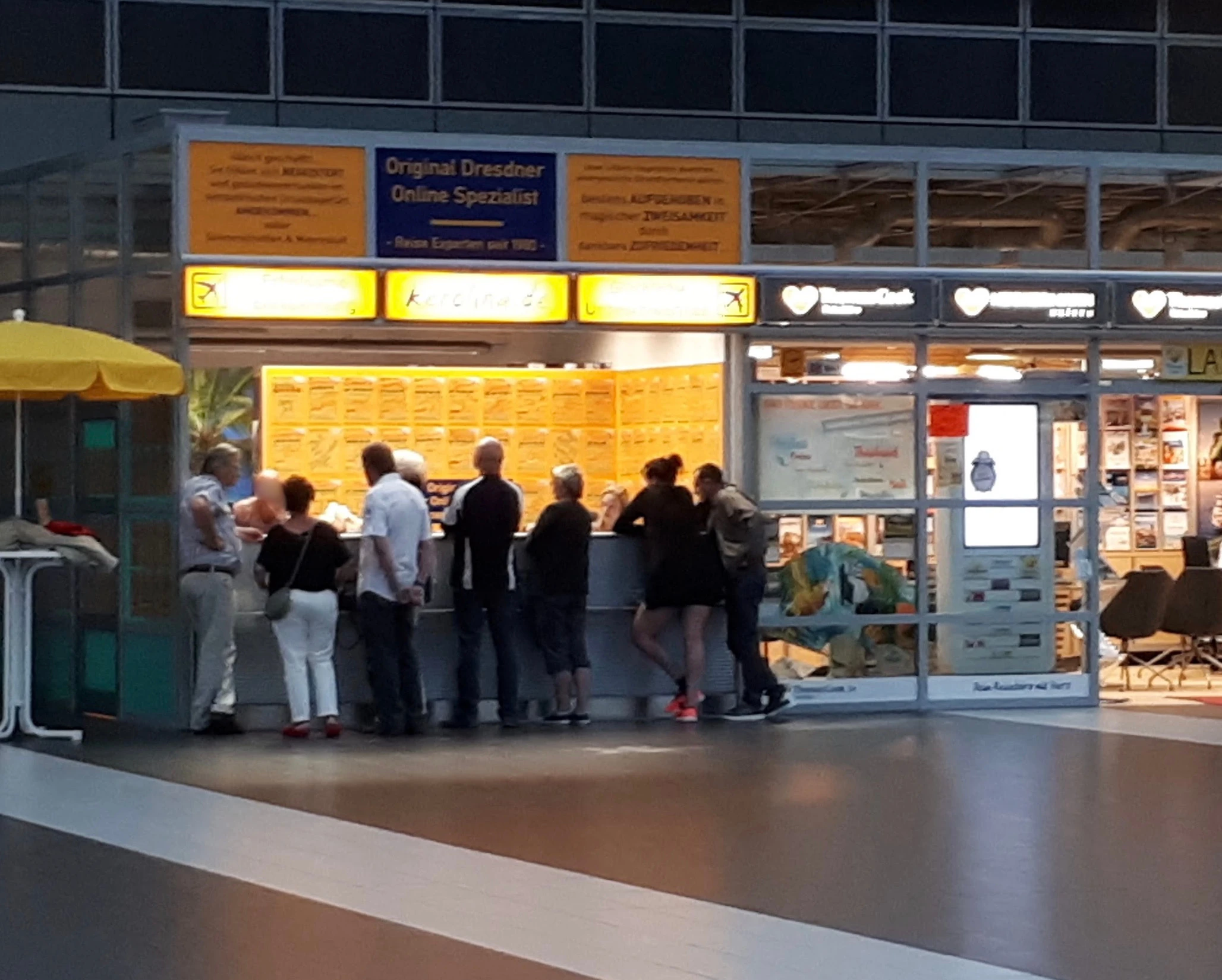Abendliche Szene am KEROLINA-Counter im Flughafen Dresden mit mehreren Kunden, die sich beraten lassen
